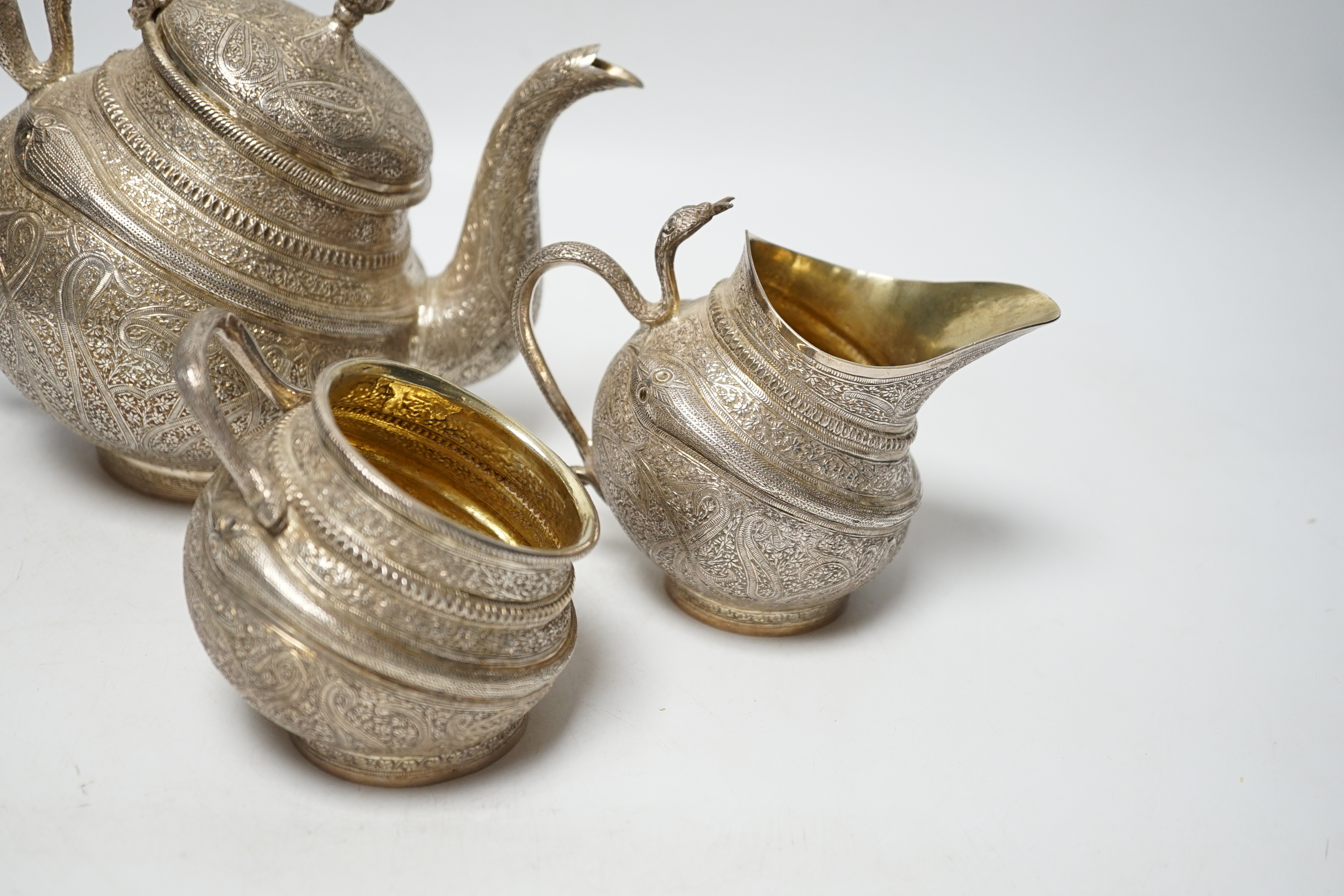 A 20th century Indian three piece embossed white metal tea set, with boteh and cobra decoration, gross weight 38.6oz.